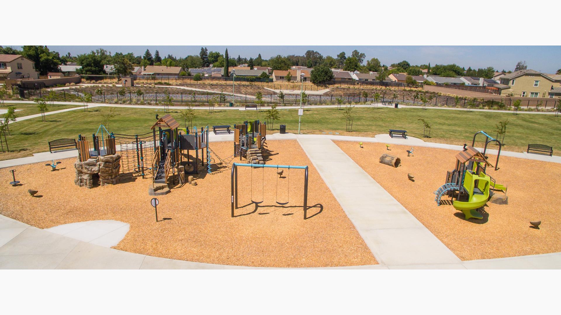 Elevated full view of a large play space with multiple play structures with rope climbers, artificial rock and log climbers, and recycle wood plank panels and roofs.