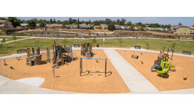 Elevated full view of a large play space with multiple play structures with rope climbers, artificial rock and log climbers, and recycle wood plank panels and roofs.