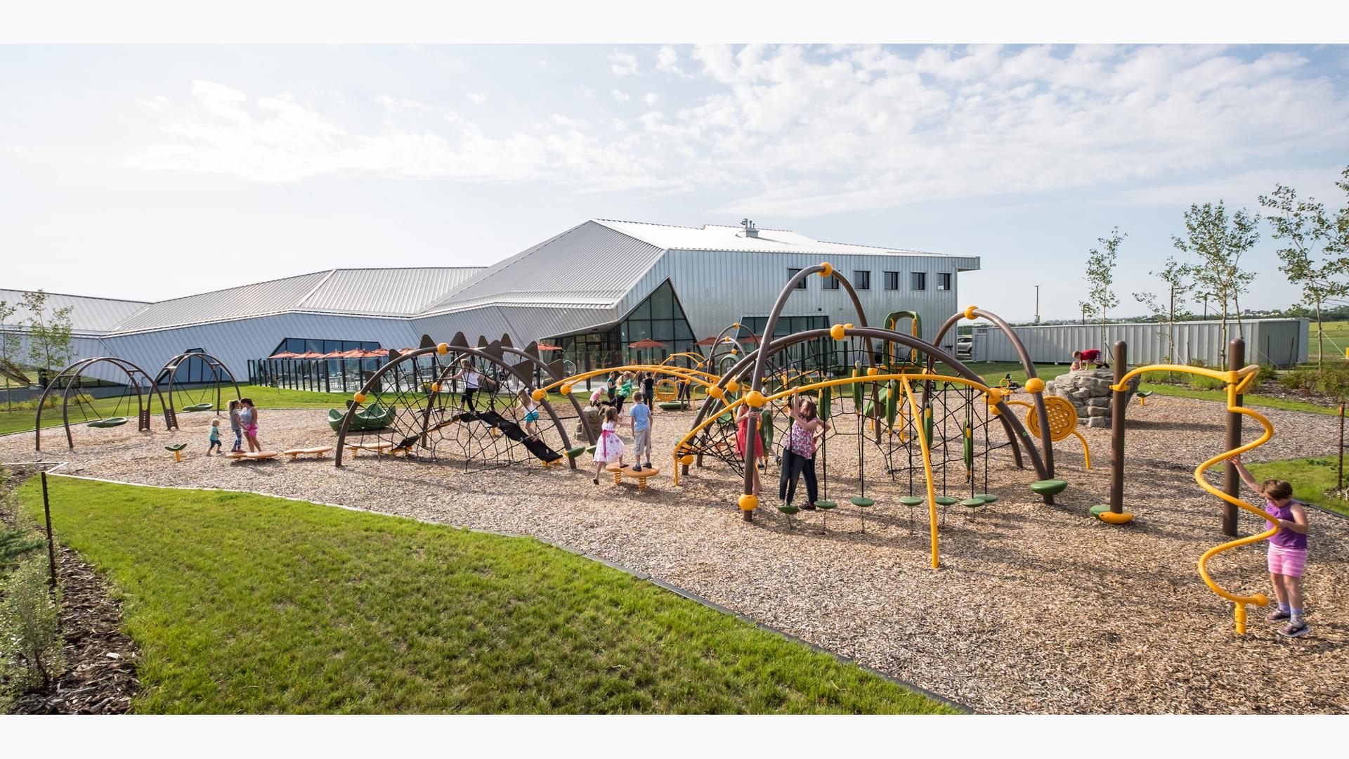 With the museum in the background, lots of kids playing on the arched-shaped playground structure-climbing, swinging, and jumping.