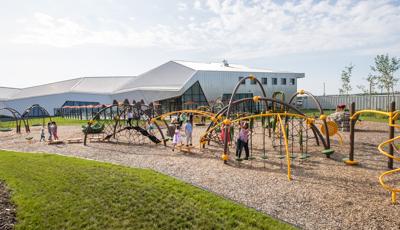 With the museum in the background, lots of kids playing on the arched-shaped playground structure-climbing, swinging, and jumping.
