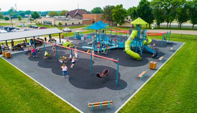 Elevated view of a church playground with inclusive surfacing, a bay of swings, large play structure with tower, and zip line rides.