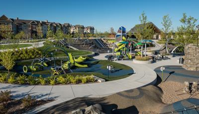 Park with several play areas including a rock climber, enclosed playground tower, climbing net climber and hillside slides with trees intermixed among the play spaces. 