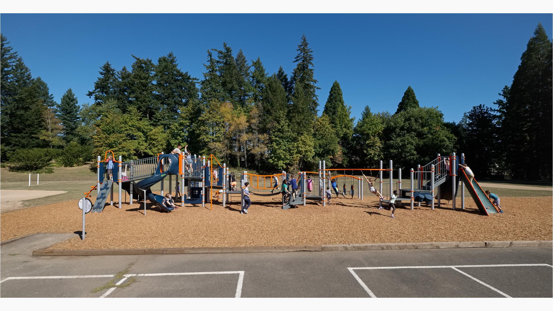 Many children playing on PlayBooster play structure. A boy and girl swing on Overhead events. Other kids play on slides climber and across bridges.