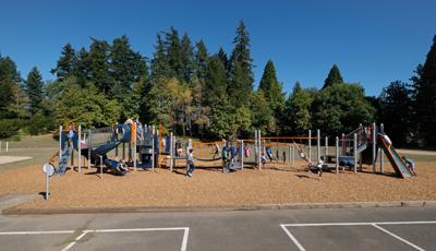 Many children playing on PlayBooster play structure. A boy and girl swing on Overhead events. Other kids play on slides climber and across bridges.