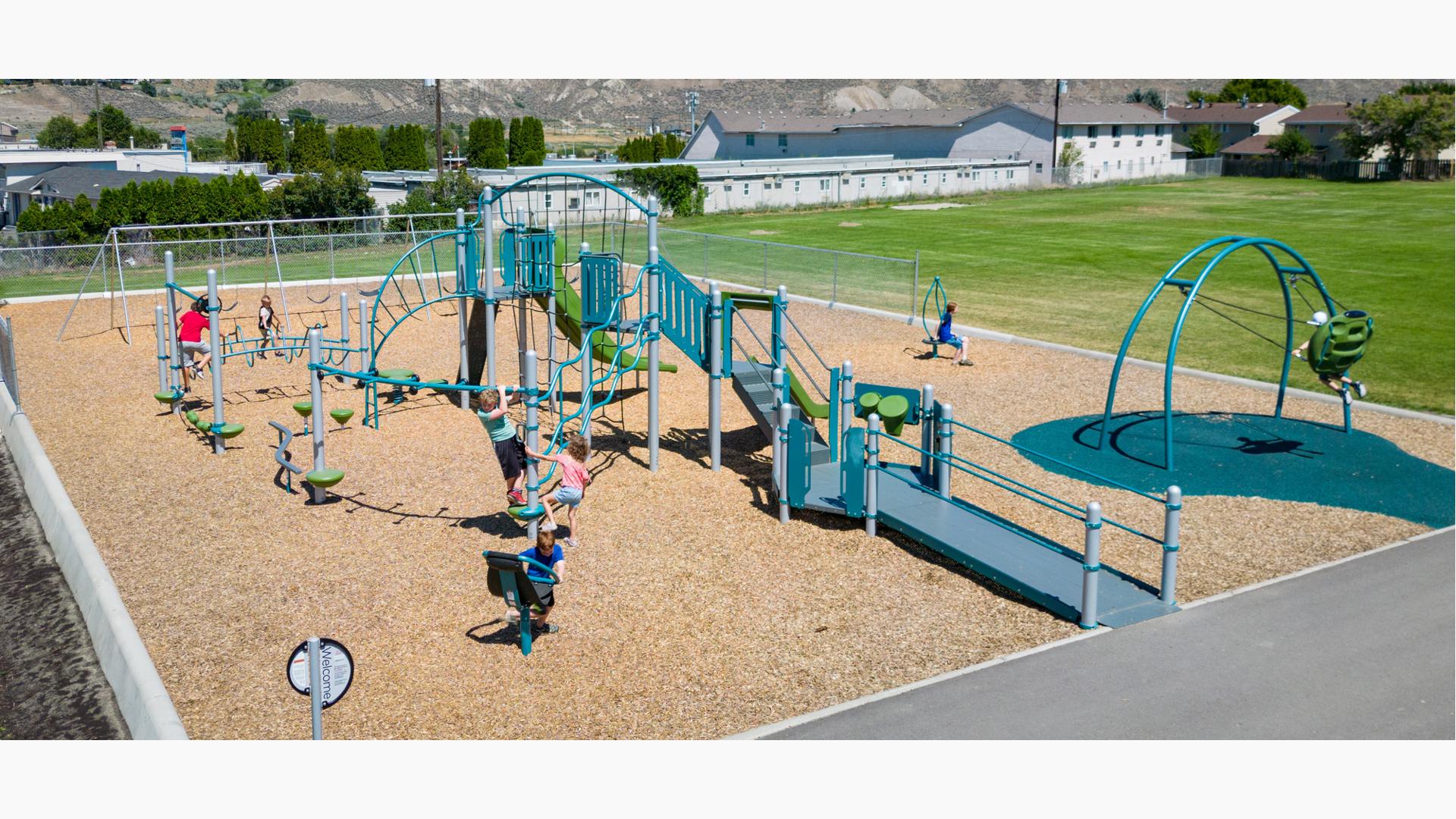 Children play on a elementary school playground next to a large open grass field.