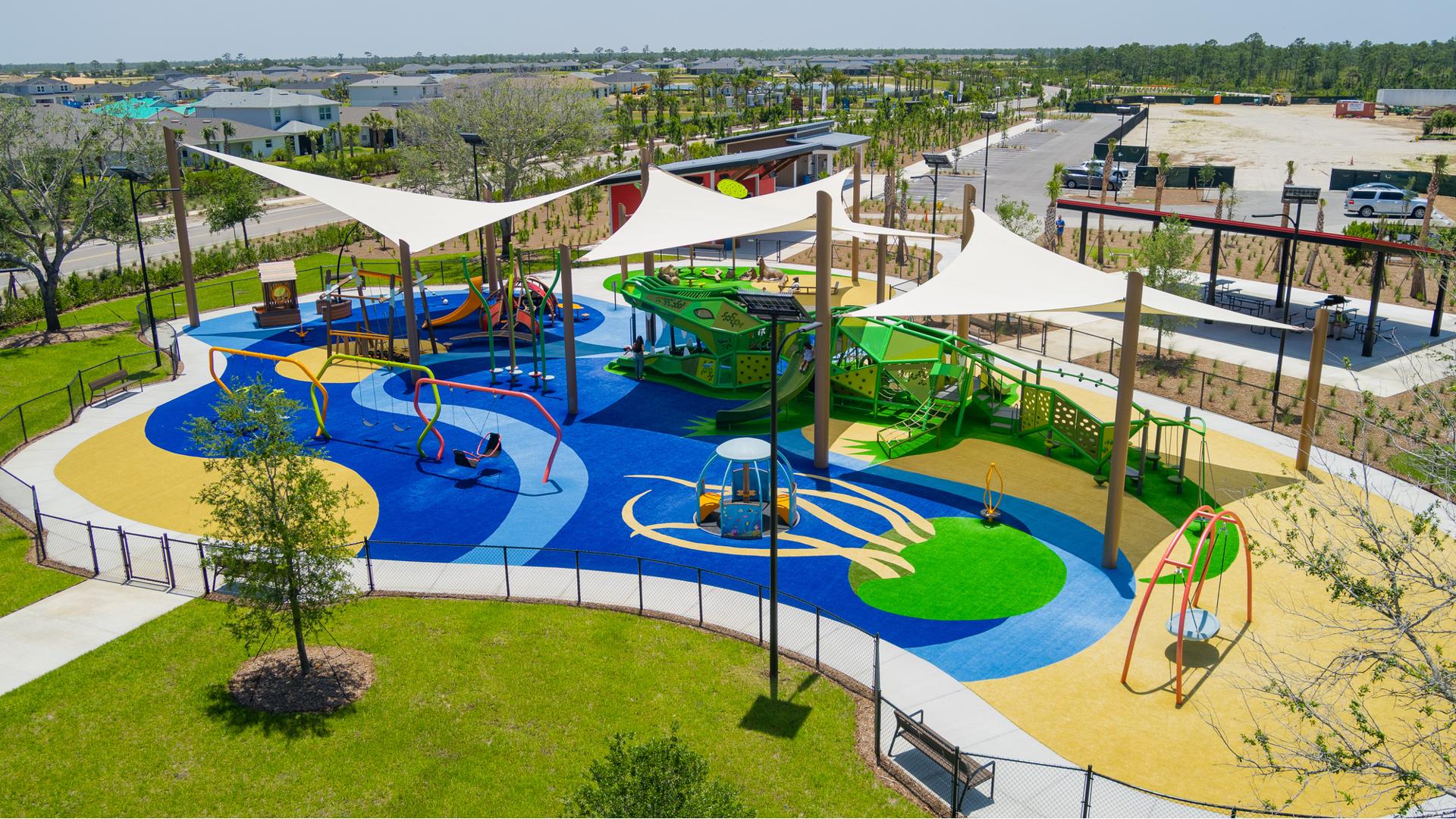 Elevated view of large shade sails cover a large water themed play area with unique crocodile play structure. 