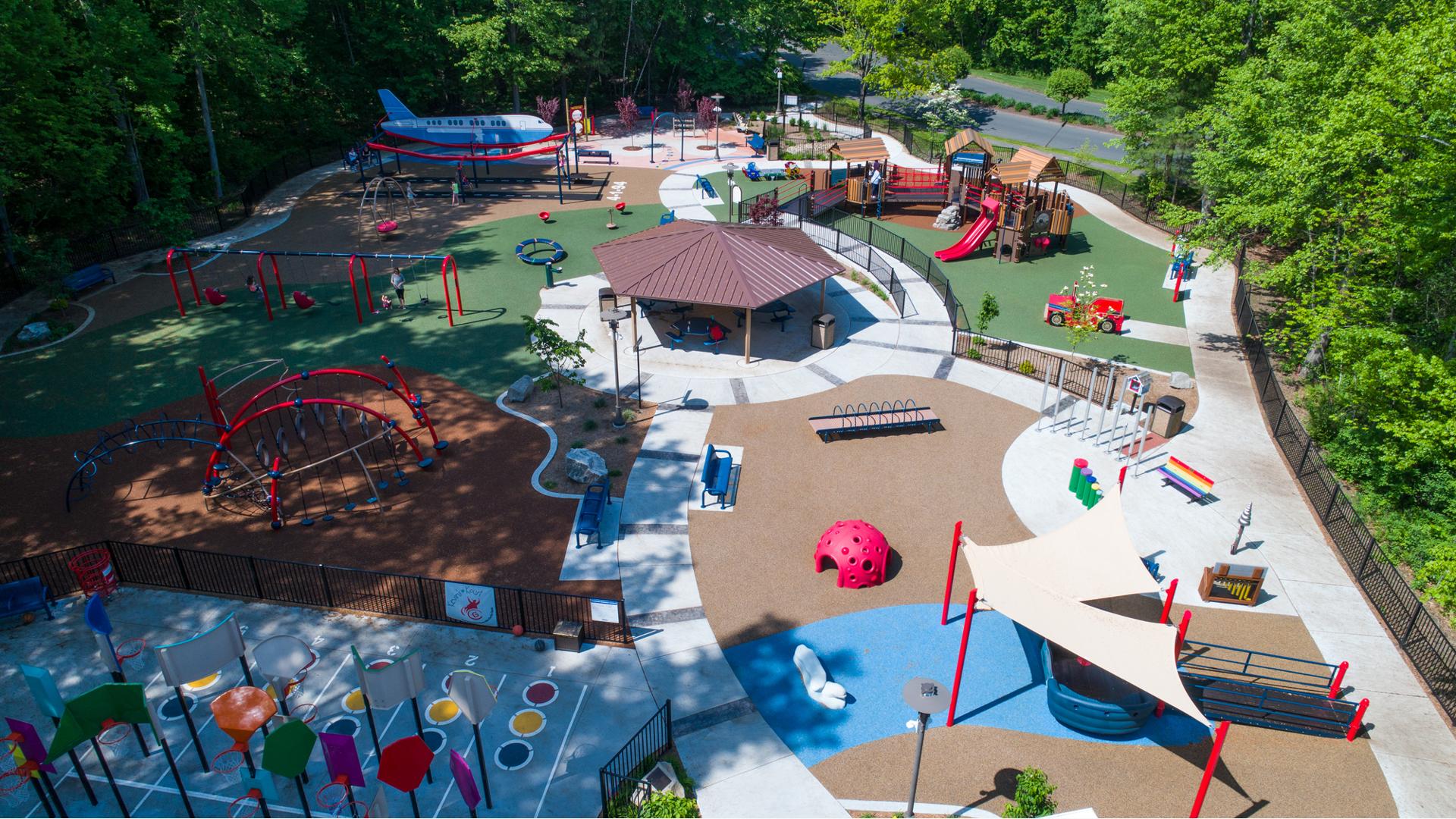 Parent pushes their child on swing in sprawling Jonathan's Dream Reimagined park. Surrounded by forest, the park offers something for every child of all ages and abilities.