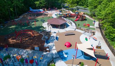 Parent pushes their child on swing in sprawling Jonathan's Dream Reimagined park. Surrounded by forest, the park offers something for every child of all ages and abilities.