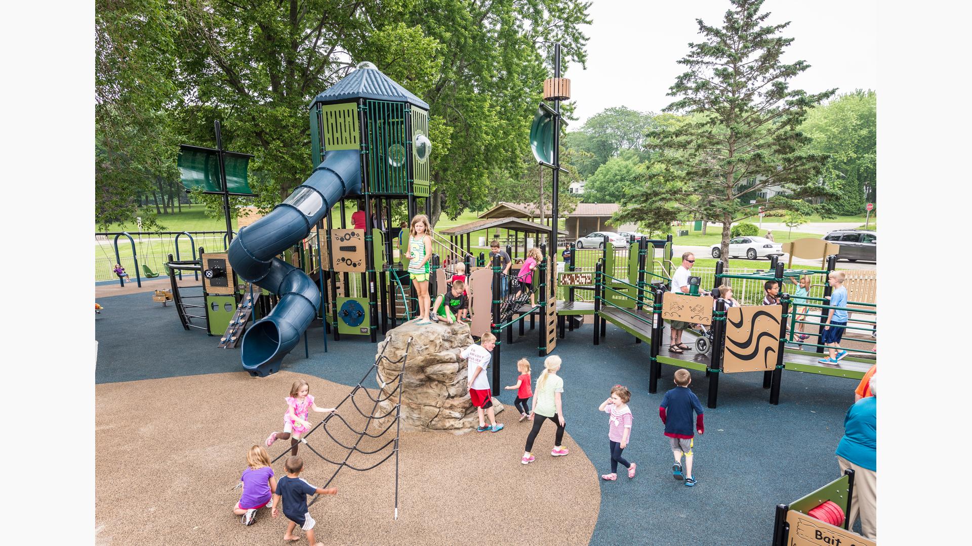 Ship-themed custom PlayBooster play structure with children of all abilities using the ramps to get around. Nature-inspired Adventurescapes climber leads to net below.