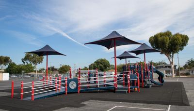 A inclusive school playground with accessible ramps, red posts and navy blue play panels, slides, climbers, and overhead shades.