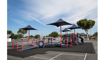 A inclusive school playground with accessible ramps, red posts and navy blue play panels, slides, climbers, and overhead shades.