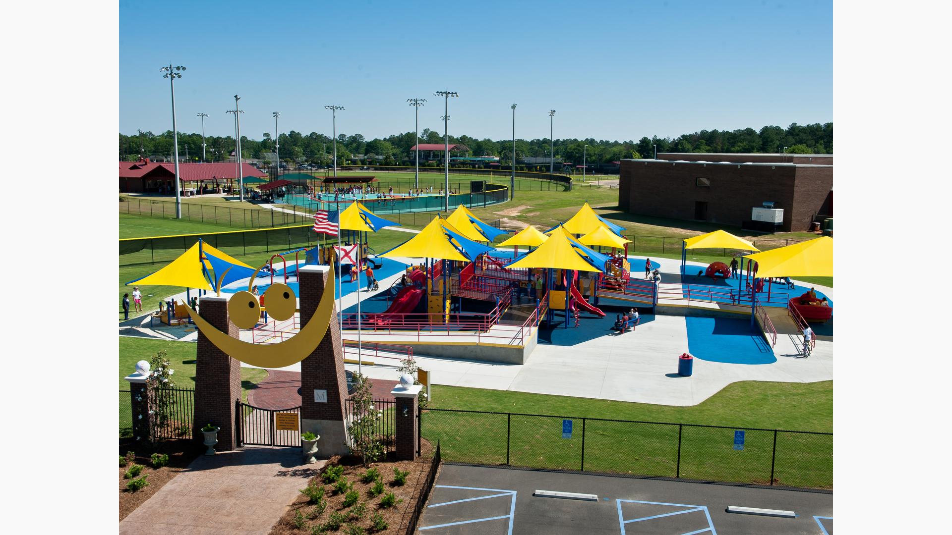 All inclusive playground covered in CoolToppers shade system with Baseball fields in background. Smiling gateway in foreground.
