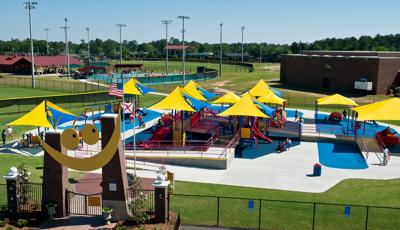 All inclusive playground covered in CoolToppers shade system with Baseball fields in background. Smiling gateway in foreground.