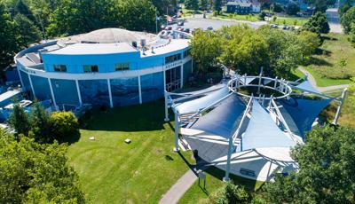 Elevated view of a circular building with a custom matching circular shade system made up of triangular shade sails colors in navy and white blue covering a courtyard sitting area.