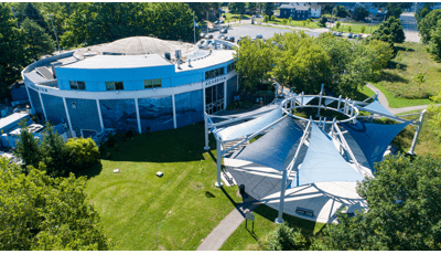 Elevated view of a circular building with a custom matching circular shade system made up of triangular shade sails colors in navy and white blue covering a courtyard sitting area.