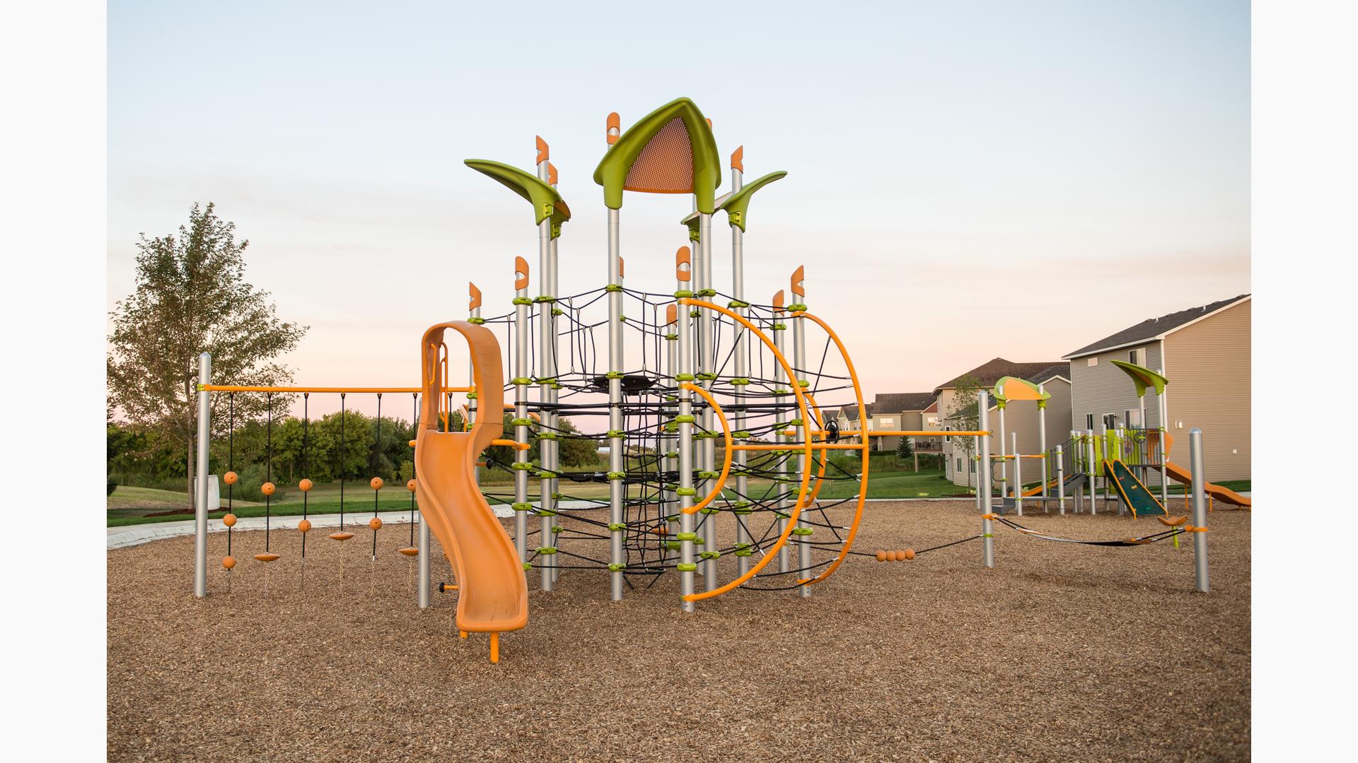 A neighborhood park playground with a post tower playground equipped with connecting webbed climbing ropes and a gold slide.