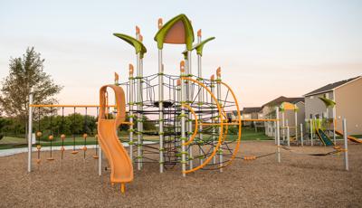 A neighborhood park playground with a post tower playground equipped with connecting webbed climbing ropes and a gold slide.