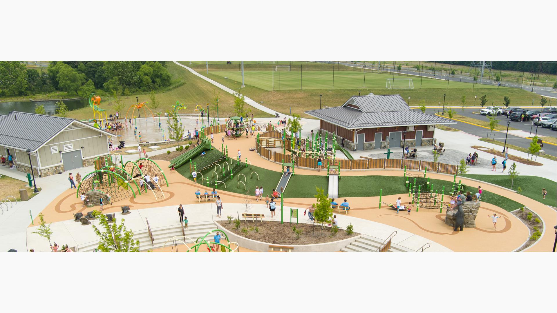 Elevated view of a large elongated park with artificial grass in the shape of a curved blade of grass with scattered play structures and activities all around the park.