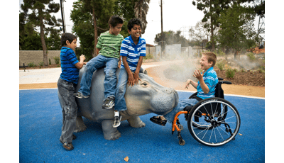四个孩子在一只会喷水的河马上玩耍。其中一个坐在轮椅上的人笑成河马。