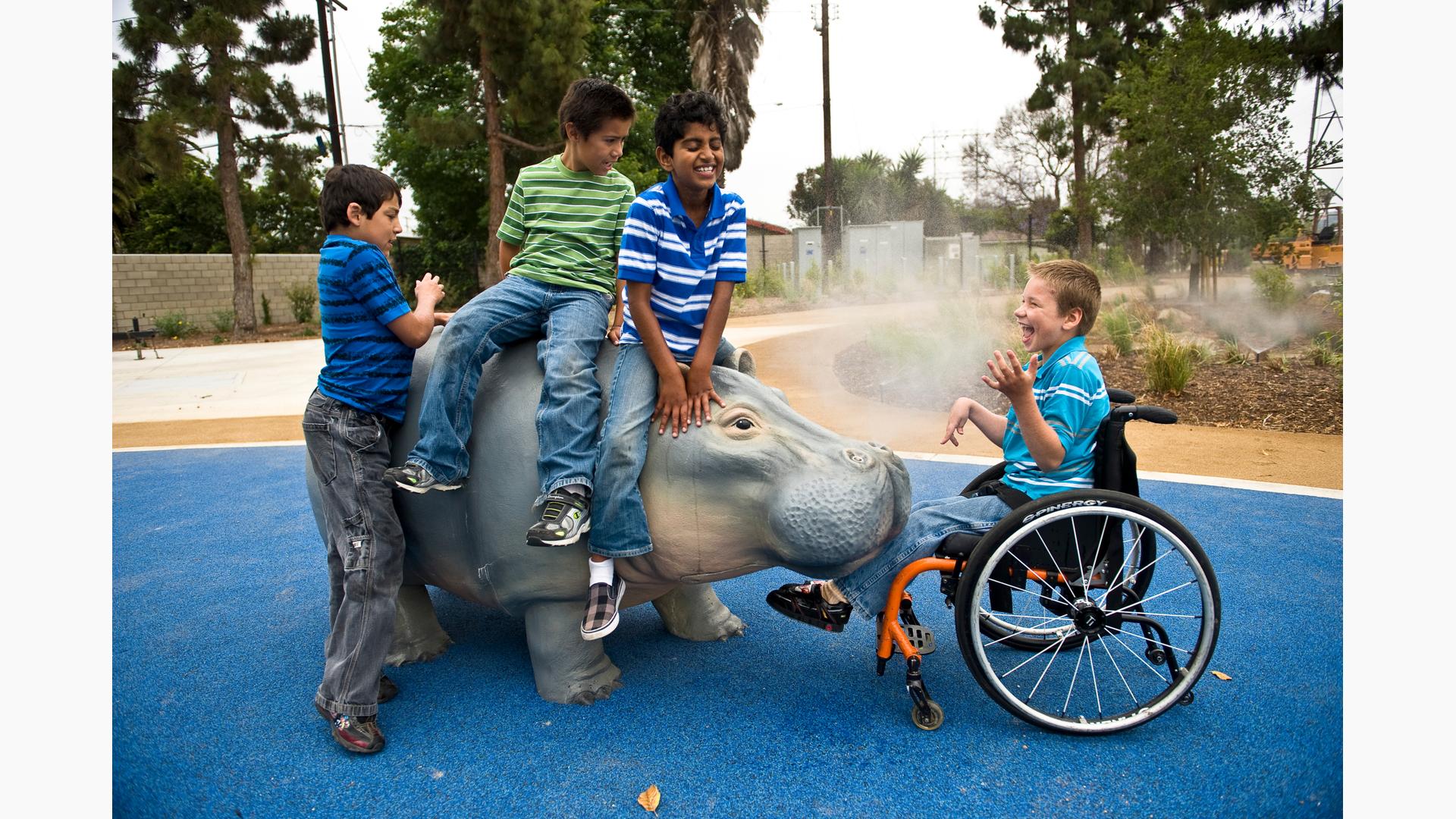 Four children play on a Hippo that sprays water. One of them who is in a wheelchair laughs as the Hippo.