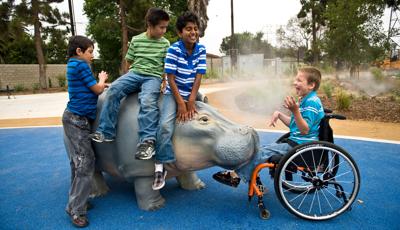 Four children play on a Hippo that sprays water. One of them who is in a wheelchair laughs as the Hippo.