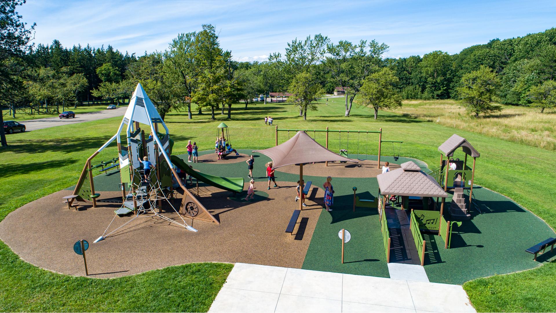 Elevated view of a town park with a playground structure on the left with a mountain theme and an additional inclusive structure on the right.