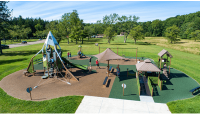 Elevated view of a town park with a playground structure on the left with a mountain theme and an additional inclusive structure on the right.