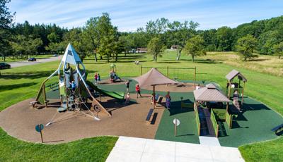 Elevated view of a town park with a playground structure on the left with a mountain theme and an additional inclusive structure on the right.