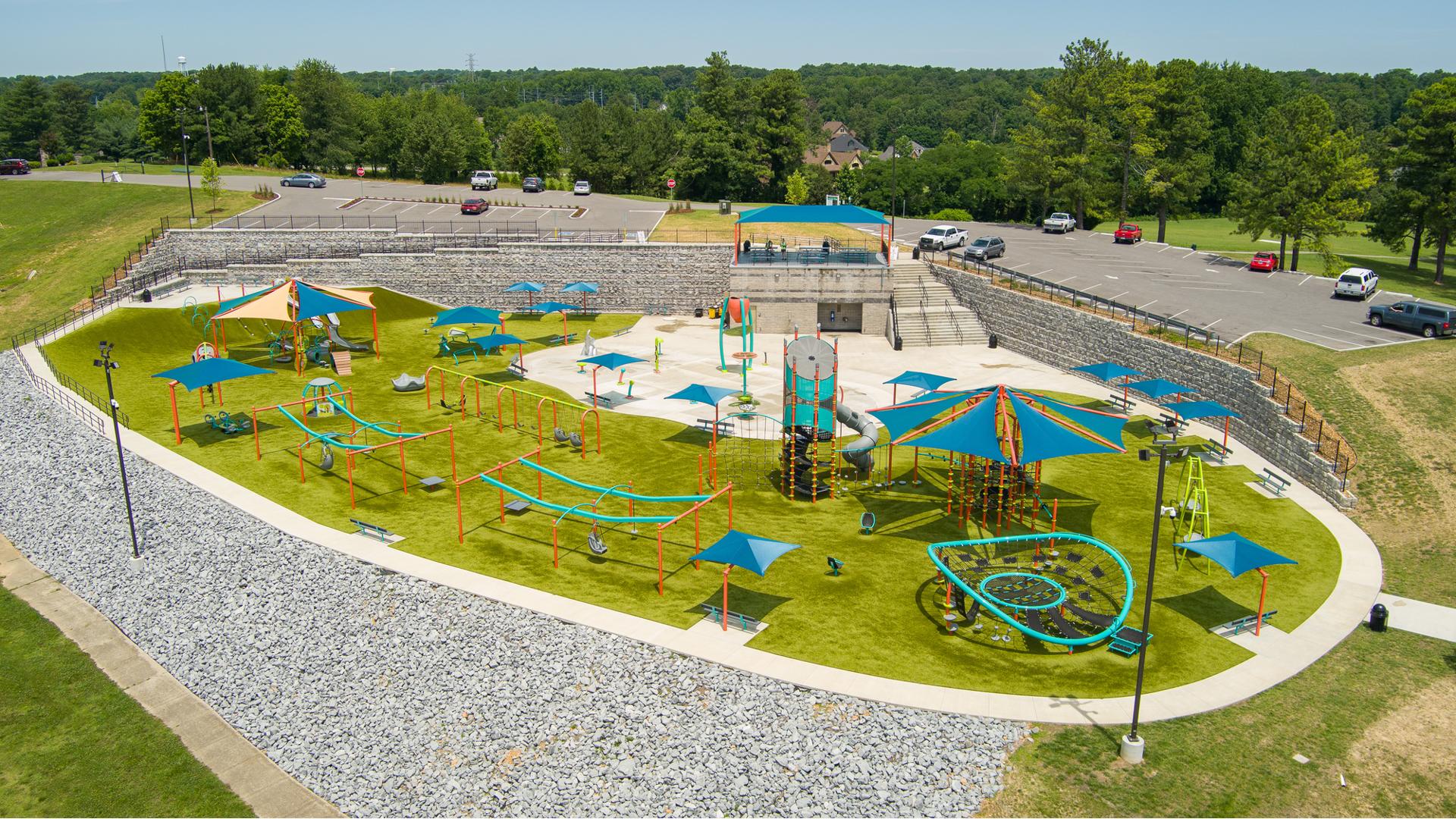 Full elevated view of a large play space filled with different playground activities, shaded seating areas and a central splash pad.