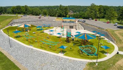 Full elevated view of a large play space filled with different playground activities, shaded seating areas and a central splash pad.