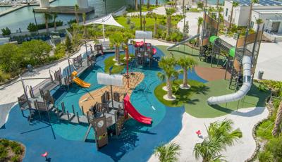 Elevated view of a boat/ocean themed playground with two separate play structures one designed as a boat while the other is a unique two tower structure connected by a elevated crawl tunnel.