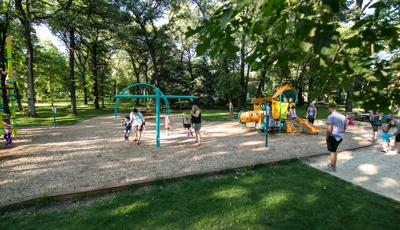 Families playing in Wildwood Park. Mothers pushing their toddlers on swings while a dad watches his child play on a Smart Play play structure.