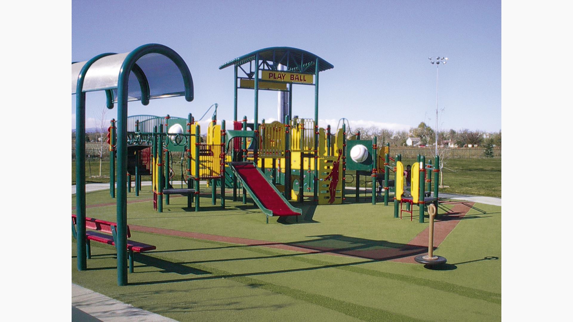 A playground with a color scheme of green, red, and yellow with additional baseball themed designs all at a sports complex. 
