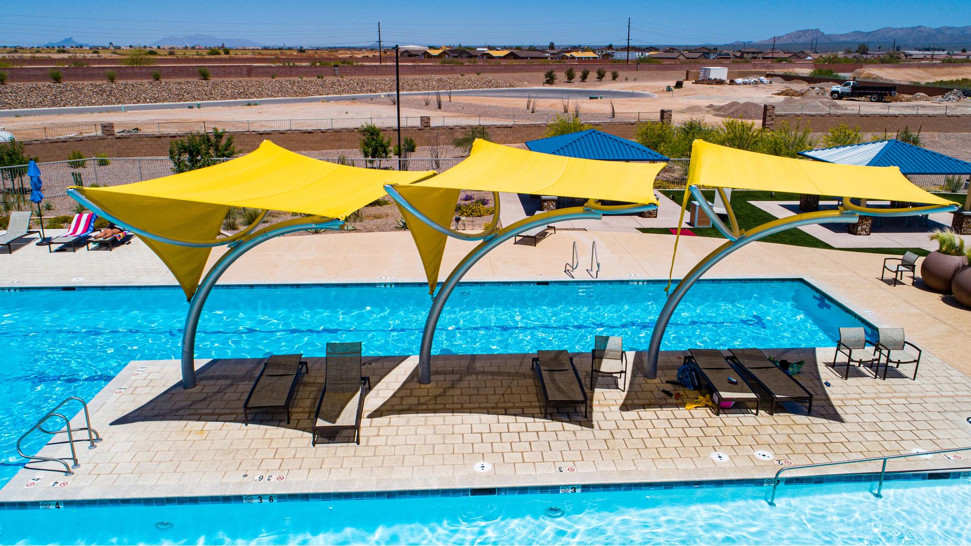 Three bright yellow shade structures covering lounge chairs in pool area. 