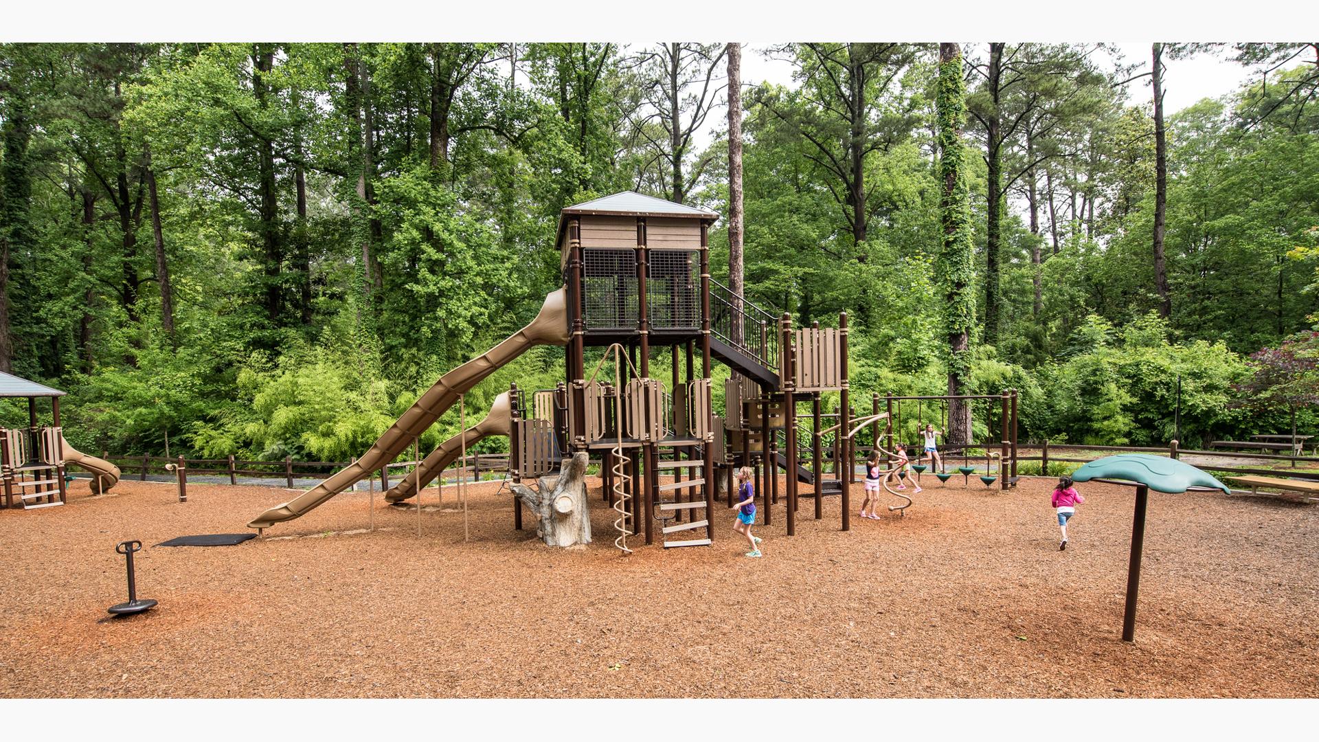 Surrounded by trees, kids play on a custom nature-inspired playground design.