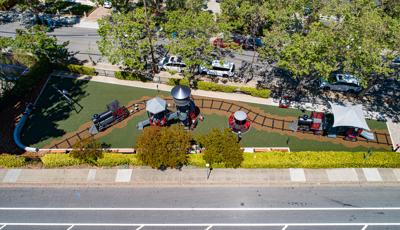 Full bird's eye view of a long and narrow play area with train designed play structures on train track designed playground surfacing. 