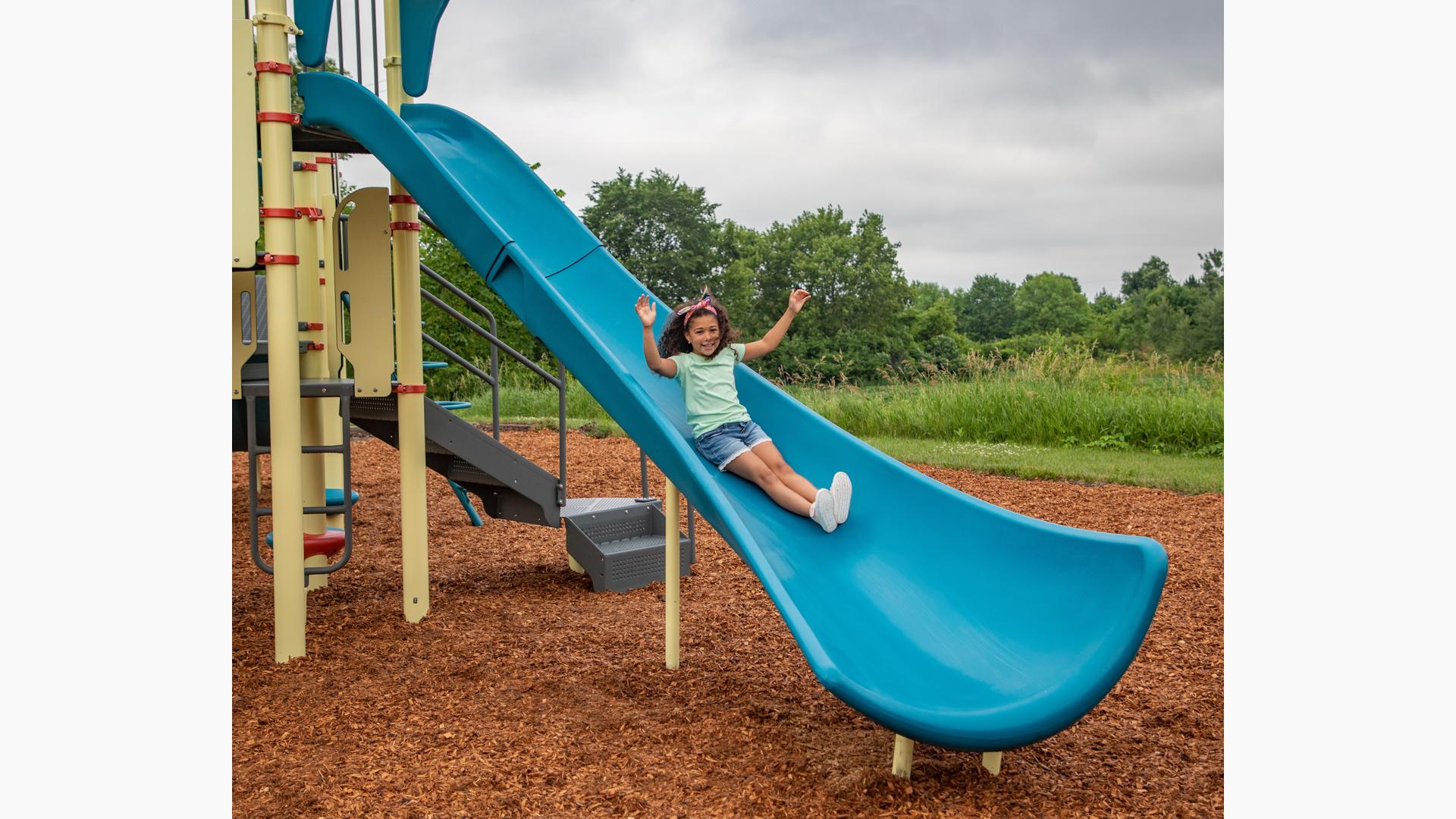 A girl puts her hands up on a playground as she descends a blue Alpine Slide.