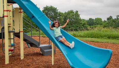A girl puts her hands up on a playground as she descends a blue Alpine Slide.