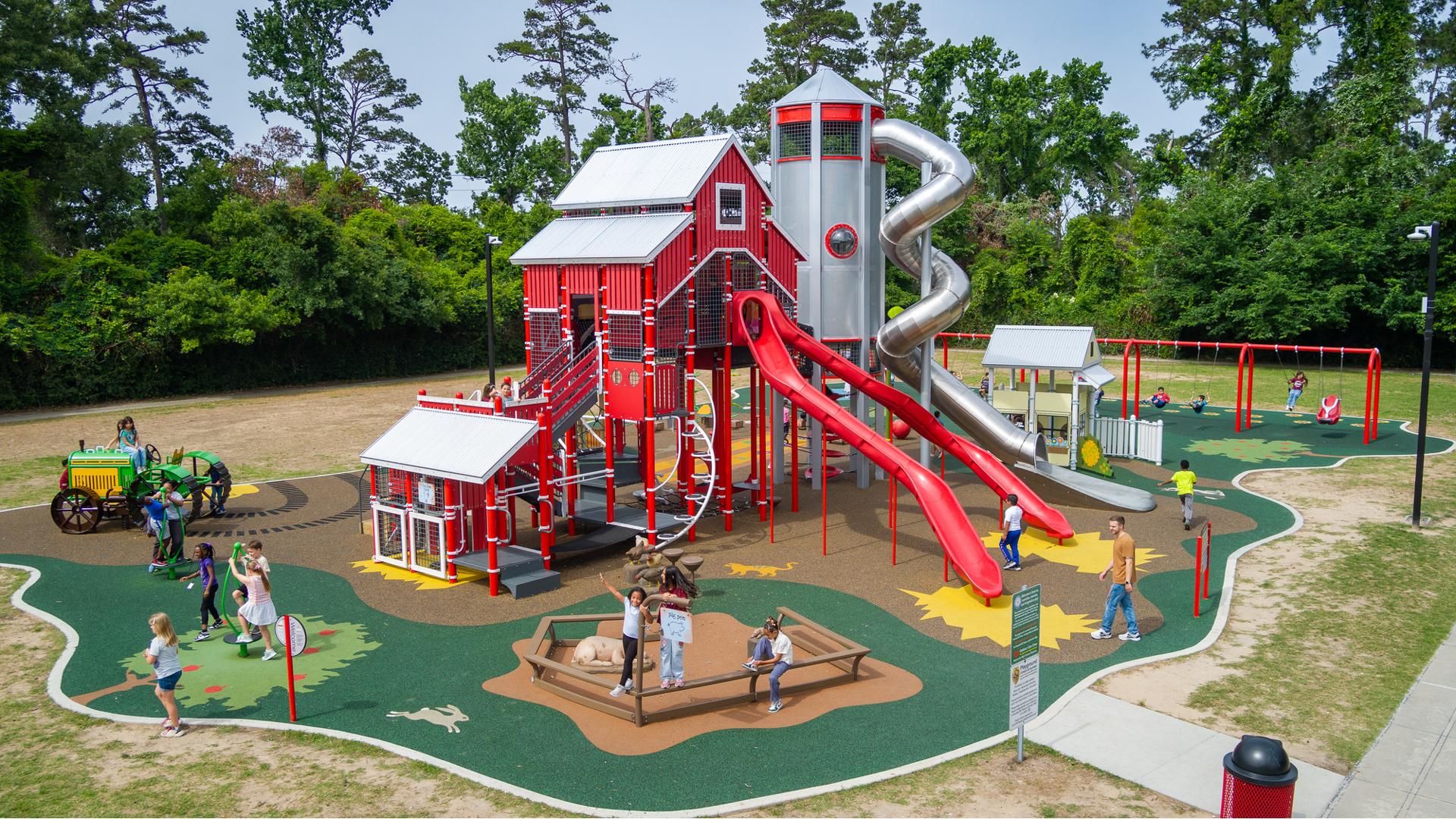 A playground with a large play structure designed like a big red barn surrounded by other farm themed play activities.