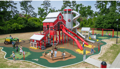 A playground with a large play structure designed like a big red barn surrounded by other farm themed play activities.