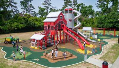 A playground with a large play structure designed like a big red barn surrounded by other farm themed play activities.