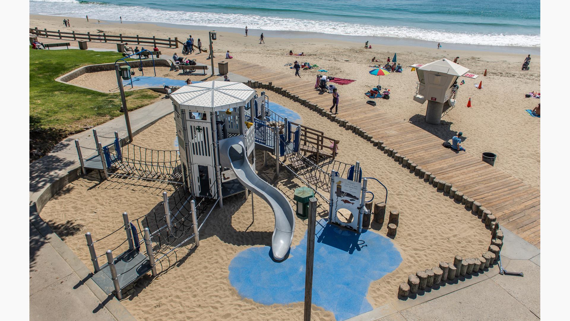 Lifeguard-themed playground tower situated along the beach with the crashing ocean waves in the background. 