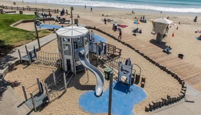 Lifeguard-themed playground tower situated along the beach with the crashing ocean waves in the background. 
