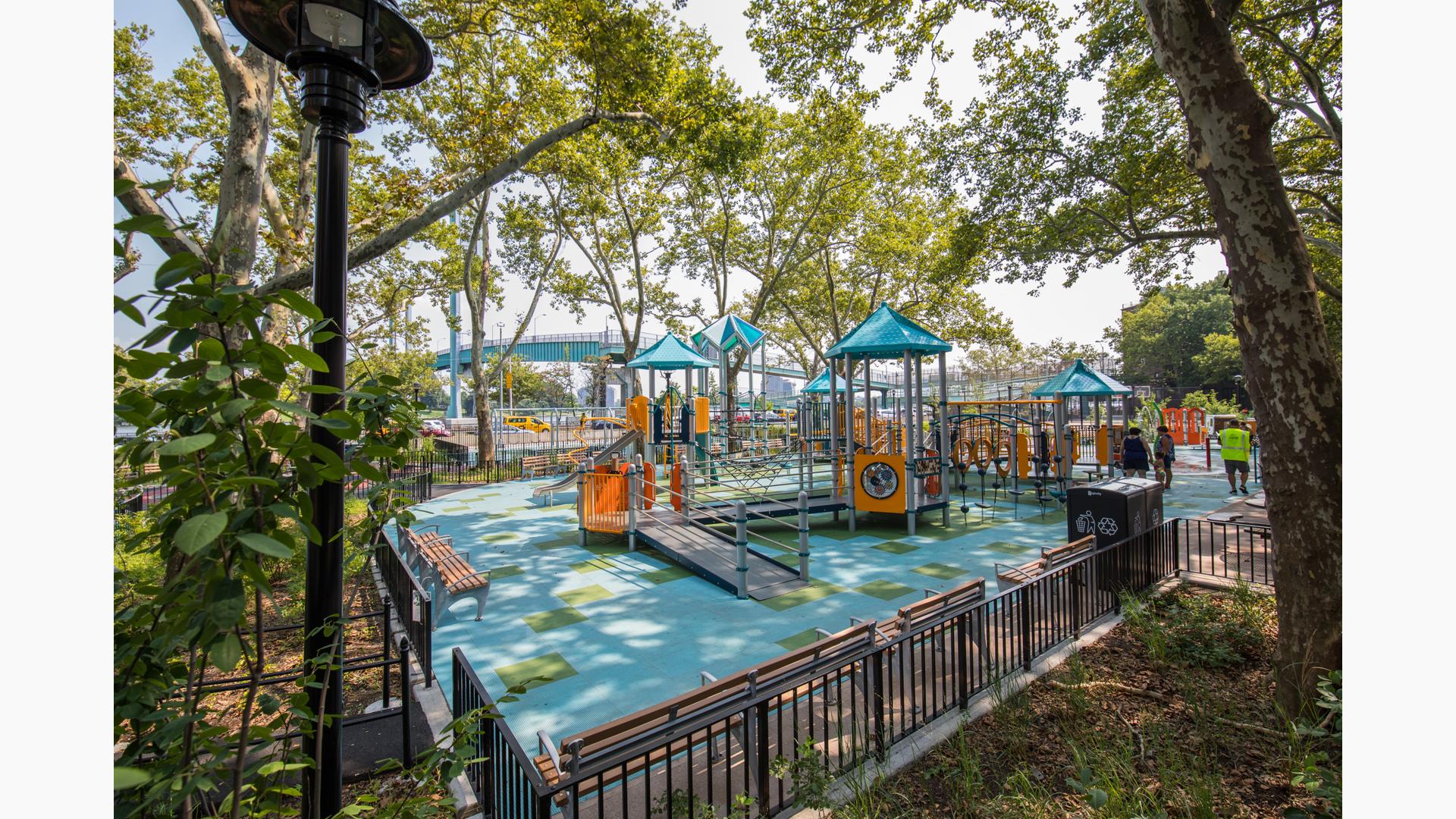 To woman stand next to play structure, which rests under the surrounding trees.