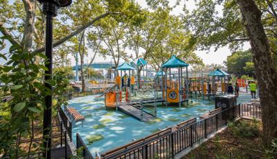 To woman stand next to play structure, which rests under the surrounding trees.