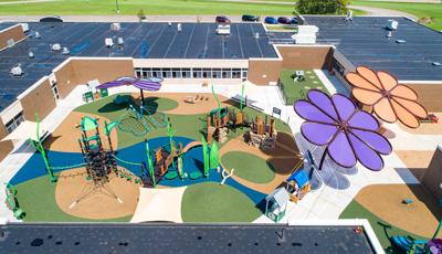 Elevated view of a nature themed central playground surrounded by a school building equipped with two large flower shaped shade systems.