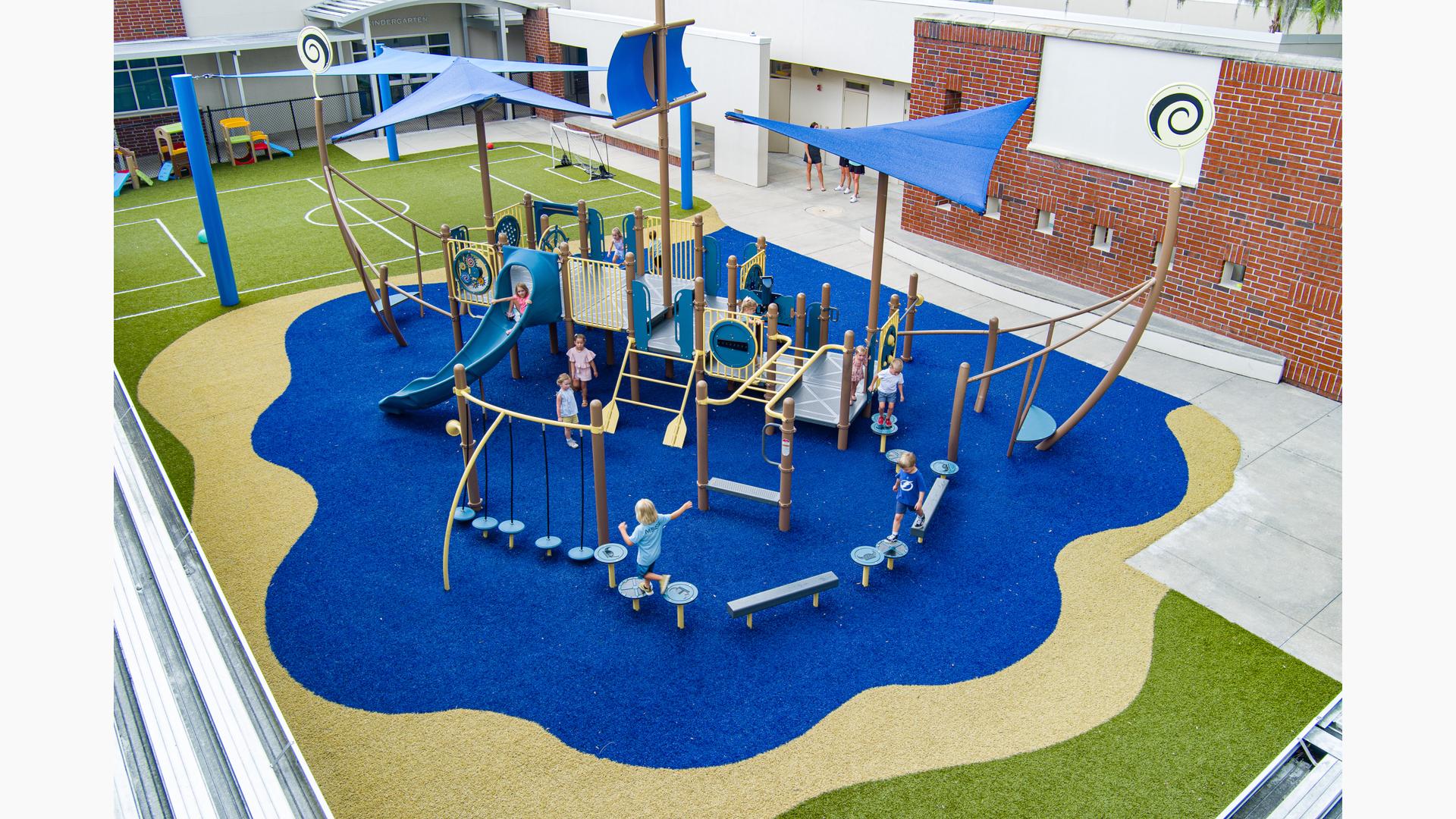 Elevated view of a play structure that looks like a ship on the water next to a school building.