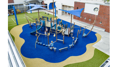 Elevated view of a play structure that looks like a ship on the water next to a school building.