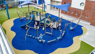 Elevated view of a play structure that looks like a ship on the water next to a school building.