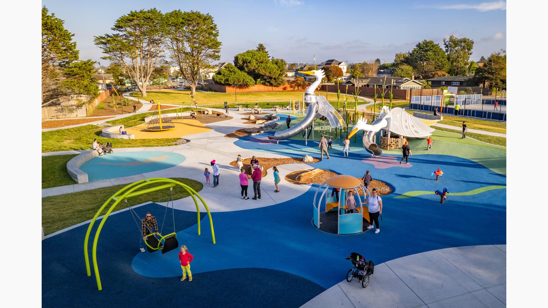 Elevated view of families playing at a park playground with the main play structure designed like large white birds.